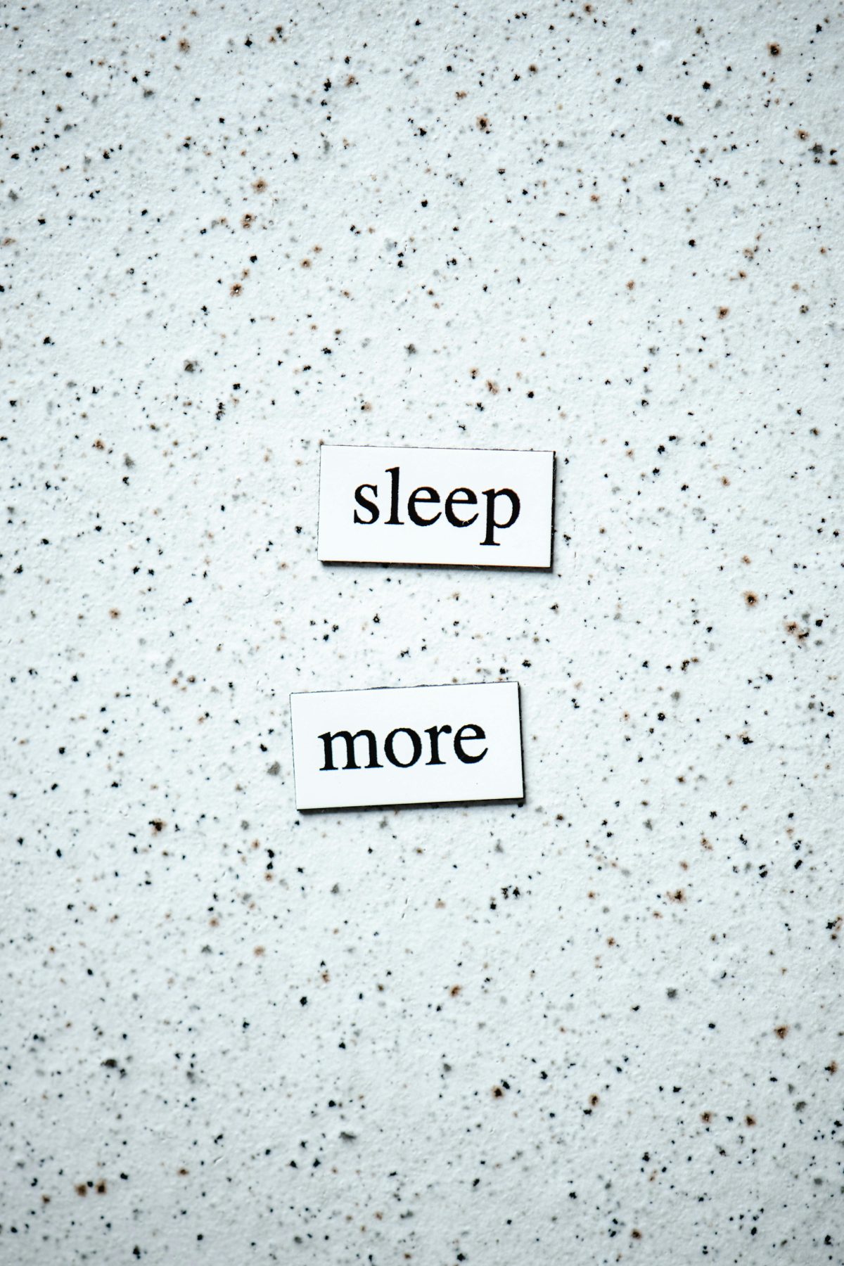 Motivational quote 'sleep more' on a minimalist speckled surface.